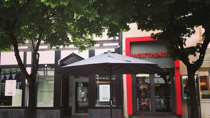 Blick auf den Eingangsbereich des Kinos Welttheater Einbeck - davor ein  Sonnenschirm